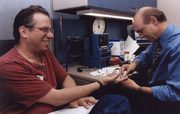 photo of Dr. Harvey Alter pricking the finger of Herb Guggenheim prior to donating blood