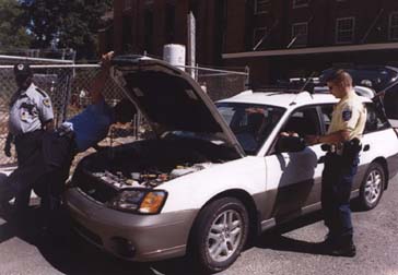 photo of several security officers and NIH police officers checking a white Subaru station wagon before entering the P3 parking garage