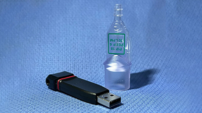 A USB flash drive (front) next to the 3D-printed miniature ventilator (back).