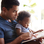 man with small child in lap reading together
