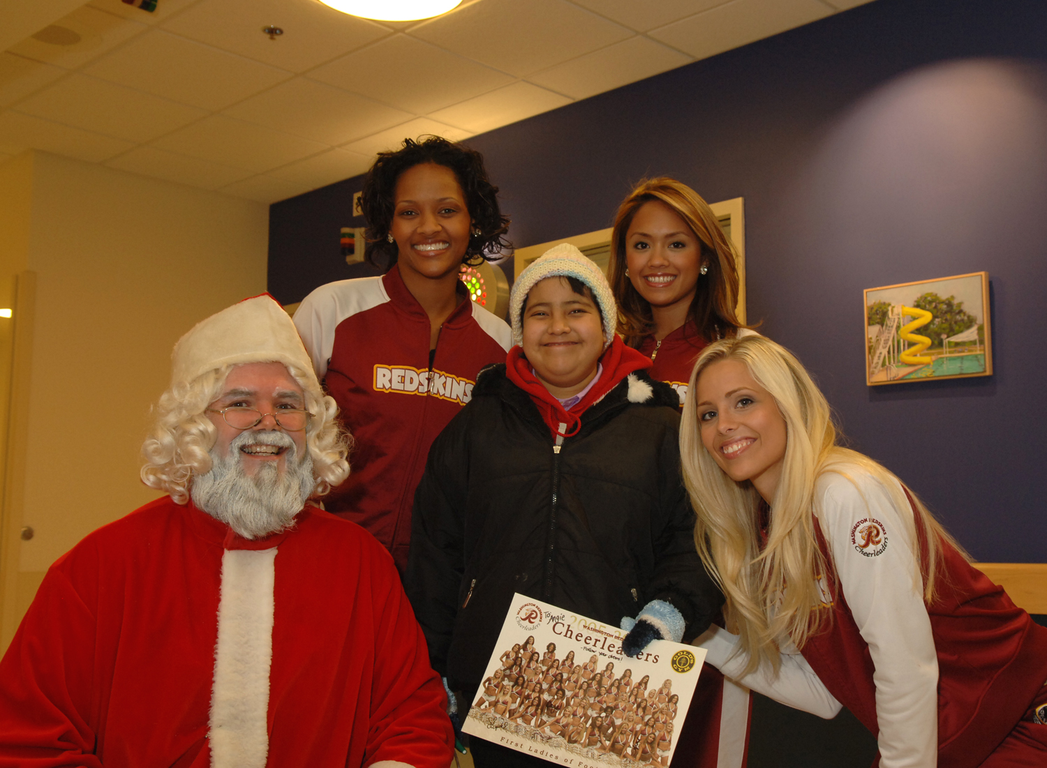 Santa Claus and the Washington Redskins cheerleaders bring some holiday cheer to Clinical Center patients, including Angie Perez Ochoa (center). Each year, the NIH police and fire departments collect donated toys and arranges for Santa to bring them to patients in need of a holiday surprise.