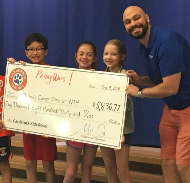 Four students and a teacher hold an oversized check to benefits patients at the NIH Clinical Center
