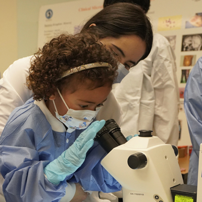 a child in a lab coat using a microscope