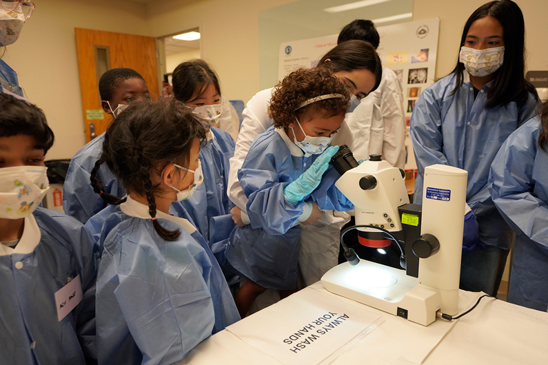 Children in lab coats use a microscope
